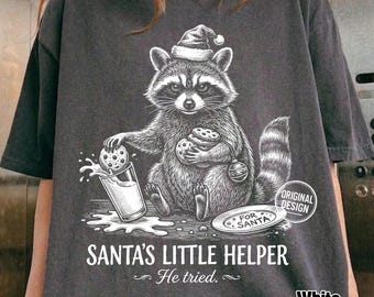 Może przedstawiać: Ciemnoszary t-shirt z białą grafiką szopa pracza w czapce Mikołaja, trzymającego ciasteczka i szklankę mleka. Napis głosi SANTA'S LITTLE HELPER He tried. Mały talerzyk jest podpisany FOR SANTA, a pieczątka zawiera napis ORIGINAL DESIGN.
