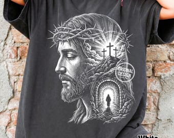 Może przedstawiać: Ciemnoszary t-shirt z białą grafiką przedstawiającą profil Jezusa w koronie cierniowej. Wzór zawiera trzy krzyże na wzgórzu, kamienny tunel z postacią idącą w stronę światła oraz napis Original Design.