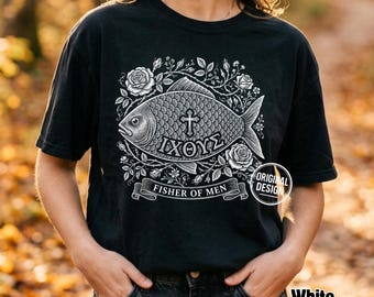 Może przedstawiać: Czarny t-shirt z białą grafiką ryby z symbolem krzyża i greckim tekstem IXΘYΣ. Wzór otoczony jest ilustracjami róż i zawiera wstęgę z napisem FISHER OF MEN oraz okrągłą pieczęć z napisem ORIGINAL DESIGN.
