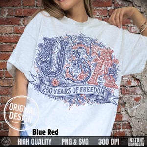 May include: A light gray t-shirt featuring a patriotic design with the word "USA" in blue and red, adorned with floral details. The text "250 YEARS OF FREEDOM" is displayed on a banner below the word "USA".