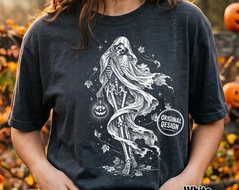 Może przedstawiać: Ciemnoszary t-shirt w kolorze antracytu z białą grafiką przedstawiającą szkielet w powiewającej pelerynie z kapturem. Szkielet trzyma świecącą dynię, otoczony opadającymi jesiennymi liśćmi, gwiazdami oraz okrągłą odznaką z napisem ORIGINAL DESIGN.