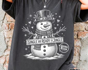 Może przedstawiać: Ciemnoszary t-shirt z białą grafiką mrugającego bałwana w cylindrze i szaliku. Bałwan trzyma drewnianą tabliczkę z napisem "SINGLE AND READY TO JINGLE", otoczoną małymi serduszkami, płatkami śniegu i gwiazdkami na całej powierzchni koszulki.