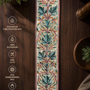May include: Handmade silk embroidered table runner rug. The cream-colored runner features a central design of teal leaves and orange berries on a vine, framed by a red border. The rug is 1/4 ft in size and has tassels on each end.