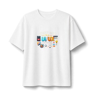May include: A white short-sleeved t-shirt featuring a central graphic with the text "TRUST ME I'M A UI/UX DESIGNER". The design includes colorful icons representing digital design tools, a smartphone, a lightbulb, and a target symbol.