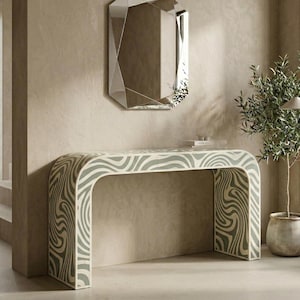 May include: A contemporary console table featuring a curved design and a distinctive wave pattern in grey and white. Above, a geometric mirror is mounted on the wall. A small potted plant is positioned to the right of the table.