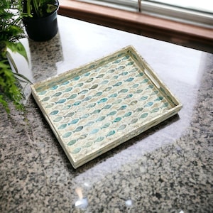 May include: Rectangular serving tray with a mosaic fish pattern in shades of blue, teal, and cream. The tray has a light-coloured wooden frame and integrated handles. The tray is suitable for serving food or as a decorative accent.