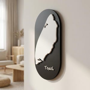 Op de afbeelding: Een verticaal ovaal wandbord met een donkergrijze achtergrond en een verhoogde witte kaart van het eiland Texel. Het woord Texel staat in witte schrijfletters rechtsonder op het bord, dat aan een muur is bevestigd.