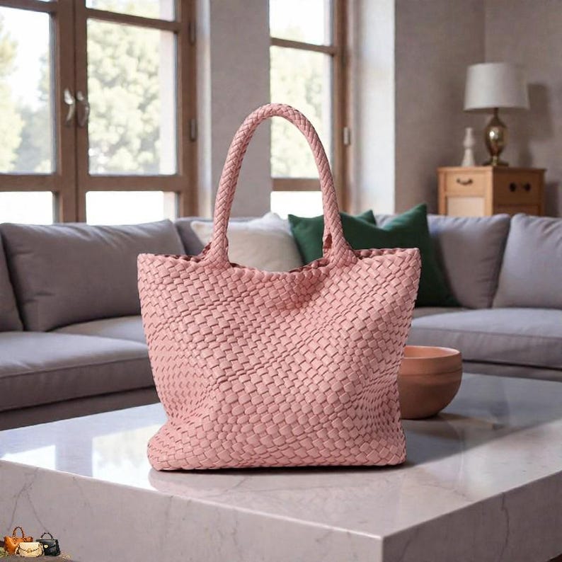 May include: A light pink woven tote bag with braided handles. The bag is rectangular with a wide base and a woven pattern. The bag is sitting on a white marble table.