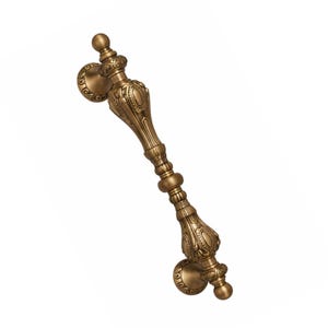 May include: Ornate bronze door handle with detailed floral and scrollwork designs. The handle features a central grip with decorative elements and rounded end pieces. The hardware is a warm, antique gold color, suitable for vintage or classic decor.