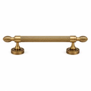 May include: A horizontal cabinet pull handle in a brushed antique brass finish. The central bar features a ribbed, fluted texture, flanked by two rounded, finial-style ends. It is supported by two circular, tiered mounting bases on each side.