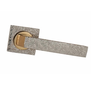 Könnte beinhalten: Silberfarbener Türgriff mit quadratischer Basis und rechteckigem Griff. Der Griff weist ein verziertes, graviertes Blumenmuster auf. Die Mitte der Basis ist goldfarben und setzt einen Kontrast zum Design.
