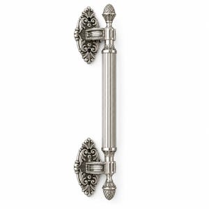 May include: A silver-toned metal door handle featuring a long, vertically fluted cylindrical grip. The handle is anchored by two ornate, oval-shaped mounting plates with intricate scrollwork and decorative finials at both ends.