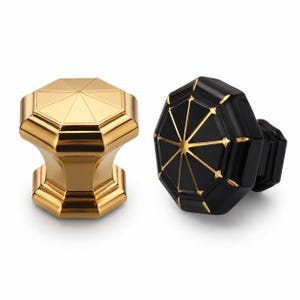 May include: Two octagonal cabinet knobs. One knob is solid polished gold with a faceted top. The second knob is matte black with gold-colored lines radiating from the center to the edges of the octagonal face, featuring a matching black base.
