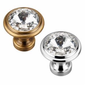 May include: Two round cabinet knobs featuring a faceted clear crystal center. One knob has an antique brass finish with a warm, brushed texture, while the other knob has a polished, reflective chrome finish. Both knobs have a circular base.