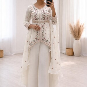 Peut inclure: Ensemble palazzo brodé de couleur ivoire. Le haut présente un col en V et des manches longues avec des broderies florales rouges, marron et vertes. Le pantalon est large. Un voile transparent ajoute de l'élégance.