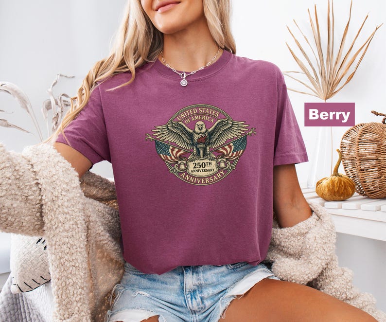May include: Berry-colored t-shirt featuring a detailed graphic of an eagle with outstretched wings, the American flag, and the text "UNITED STATES OF AMERICA 250TH ANNIVERSARY". The shirt has short sleeves and a crew neck.