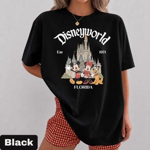 May include: Black t-shirt featuring the text "Disneyworld" above an illustration of Cinderella's castle, Mickey Mouse, Minnie Mouse, and Pluto. The text "Est 1971 Florida" is also included. The shirt is a classic crew neck.