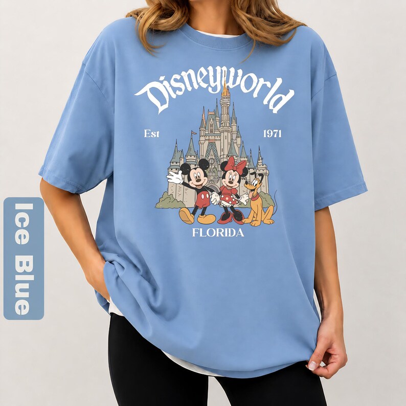 May include: Ice blue t-shirt with a Disneyworld graphic. The graphic features Mickey Mouse, Minnie Mouse, and Pluto in front of a castle. The text "Disneyworld Est 1971 FLORIDA" is printed above and below the characters.