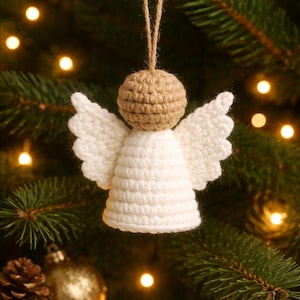 Puede incluir: Adorno navideño de ángel hecho a mano con ganchillo. El ángel tiene una cabeza beige, alas blancas y un cuerpo blanco. Cuelga de una cuerda de hilo natural. El adorno se muestra en un árbol de Navidad con luces suaves y borrosas.
