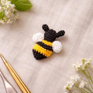 May include: A handmade crochet bee with black, yellow, and white details. The bee has a striped abdomen and white wings. The bee is a small, decorative item, possibly a brooch or applique.