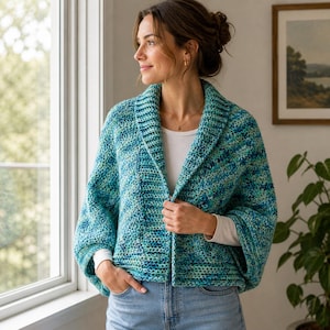 May include: A turquoise and blue crochet jacket with a shawl collar. The jacket has long sleeves and is worn open. The model is wearing a white shirt underneath and blue jeans. The jacket is made of a soft, textured yarn.