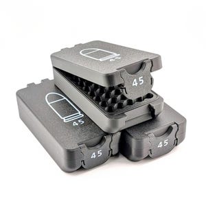 May include: Three stacked, dark gray plastic cases with hinged lids. Each case features a white outline of a bullet and the number "45". The top case is open, revealing a black interior with multiple small compartments.