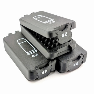 May include: Three black plastic cases, each with a hinged lid, are stacked on a white surface. The lids feature a white outline of a bullet and the number "40". One case is open, revealing a grid-like interior.