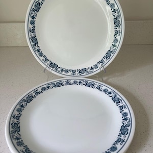 May include: A stack of white ceramic plates with a blue floral border design. The plates are round and have a simple, elegant aesthetic. The blue floral pattern adds a touch of color and visual interest to the otherwise plain white surface.