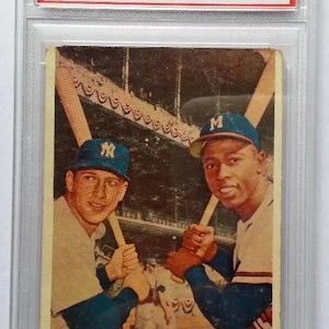 Op de afbeelding: Een honkbalkaart van 1958 van Topps met Mickey Mantle en Hank Aaron. De kaart toont de spelers met knuppels, met de tekst "WORLD SERIES BATTING FOES". De kaart is beoordeeld en in een beschermende houder geplaatst.