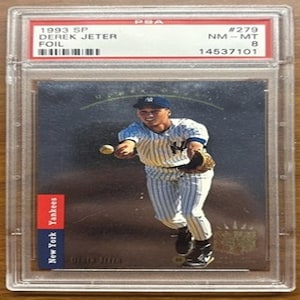 Puede incluir: Una tarjeta de béisbol de lámina de Derek Jeter SP de 1993, calificada NM-MT 8 por PSA, en un soporte protector. La tarjeta presenta una foto en color de Jeter con el uniforme de los Yankees de Nueva York.
