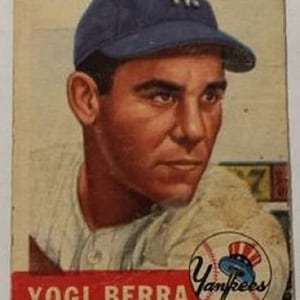 Pode incluir: Cartão de beisebol vintage com Yogi Berra do New York Yankees. O cartão mostra um retrato de Berra usando um boné azul marinho com o logotipo NY. O logotipo dos Yankees é visível no canto inferior direito, com o nome "Yogi Berra" em vermelho.