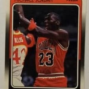 Puede incluir: Una tarjeta coleccionable de baloncesto Fleer de 1986 que muestra a Michael Jordan con una camiseta naranja de los Chicago Bulls con el número 23. La tarjeta muestra el texto MICHAEL JORDAN, FLEER, BULLS y GUARD-FORWARD, con otro jugador al fondo.