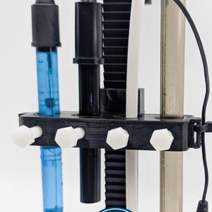 May include: A black plastic holder with various probes and tubes. The holder has white hexagonal knobs and supports a blue tube, a black tube, a white tube, and a clear tube. A logo with the text "ReefZip" is visible.