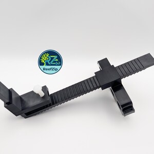 May include: Black plastic adjustable clamp with a white knob and a toothed rail. The clamp has a rectangular base and a sliding mechanism. The logo "ReefZip" is visible in the upper left corner.