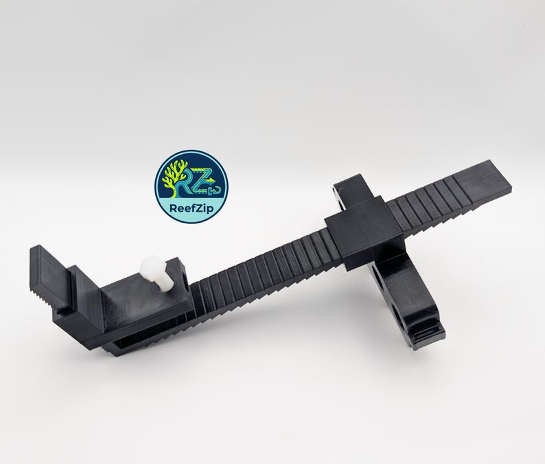 May include: Black plastic adjustable clamp with a white knob and a toothed rail. The clamp has a rectangular base and a sliding mechanism. The logo "ReefZip" is visible in the upper left corner.