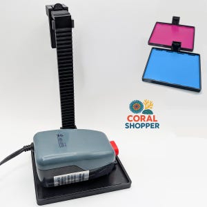 May include: A gray aquarium pump with a black vertical rack and base, featuring a power cord and a red switch. Included are two square filter frames with one pink and one blue insert. The Coral Shopper logo is visible in the center of the image.