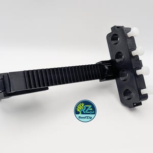 May include: A black plastic ReefZip aquarium accessory with a ridged arm and a multi-holed head with white pegs. The ReefZip logo is visible in the lower left corner. The accessory is designed for aquarium use.
