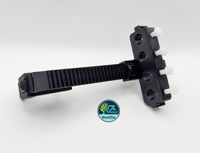 May include: A black plastic ReefZip aquarium accessory with a ridged arm and a multi-holed head with white pegs. The ReefZip logo is visible in the lower left corner. The accessory is designed for aquarium use.