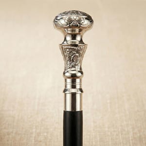 Puede incluir: Bastón plateado con un diseño floral ornamentado en el mango y un eje de madera negro. El mango tiene una parte superior redondeada con un patrón detallado. Un accesorio clásico.