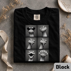 May include: A black t-shirt featuring a graphic print of six black and white photographs of a snake. The snake is shown wearing sunglasses, with its tongue out, and wearing a flower crown. The shirt has a Comfort Colors brand label at the neck.