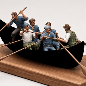May include: A miniature black boat sculpture featuring five figures in various shirts, trousers, and hats, each holding a wooden oar. The figures are positioned inside the boat, which is mounted on a rectangular wooden base, creating a detailed scene.
