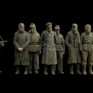 Könnte beinhalten: Eine Gruppe von Miniatur-Militärfiguren in olivgrünen und grauen Uniformen, die vor einem schwarzen Hintergrund posieren. Eine Figur hält ein Gewehr, während andere in einer Reihe stehen. Die Figuren sind detailliert und scheinen aus einer historischen Epoche zu stammen.