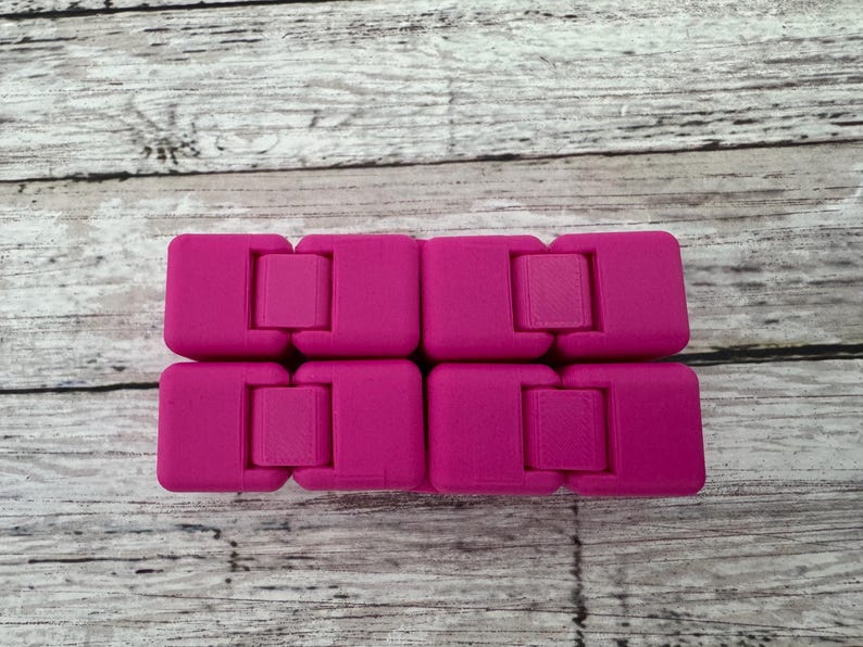 May include: A bright magenta infinity cube fidget toy composed of eight interconnected blocks. The device features a smooth, matte finish and a hinged design that allows the individual segments to fold and rotate into various geometric configurations.