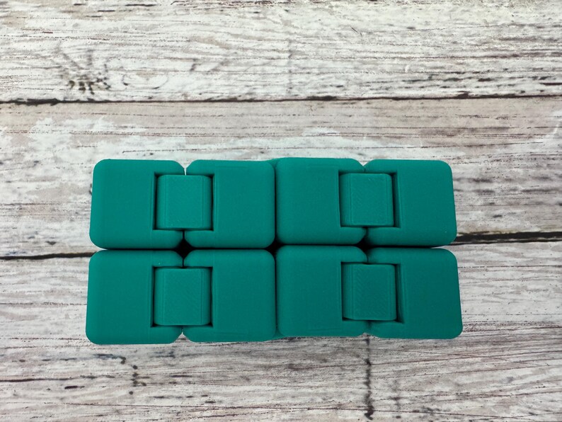 May include: A teal-colored infinity cube fidget toy composed of eight interconnected square blocks. The device features a smooth, matte finish and is designed with multiple hinges that allow the blocks to fold and rotate into various shapes.