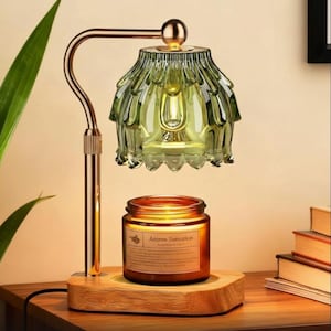 Könnte beinhalten: Aromalampe mit grünem Glasschirm und goldfarbenem Metallrahmen. Die Lampe steht auf einem Holzsockel, darunter eine Kerze in einem Glas. Das Glas trägt die Aufschrift "Aroma Sensation".