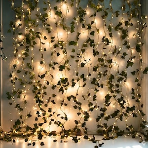 May include: A decorative string of warm white fairy lights intertwined with artificial green ivy leaves. The lights are evenly spaced, creating a soft, ambient glow. The ivy adds a natural, organic touch, suitable for home decor.