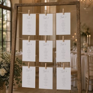 K&ouml;nnte beinhalten: Ein h&ouml;lzerner Aufsteller mit drei horizontalen Juteschn&uuml;ren. Neun wei&szlig;e, rechteckige Karten sind mit kleinen Holzklammern an den Schn&uuml;ren befestigt. Jede Karte zeigt den Text Tisch gefolgt von einer Nummer und verschiedenen Namen.
