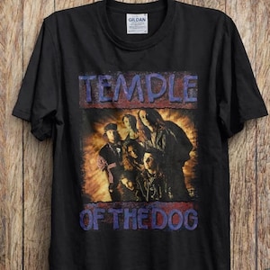 May include: Black t-shirt with the band Temple of the Dog printed on the front. The design features the band's name in blue above a group photo of the band members. The text "OF THE DOG" is below the photo.