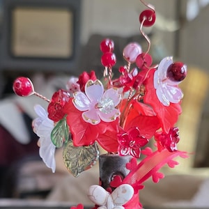 Peut inclure: Un arrangement floral décoratif avec des fleurs rouges, blanches et roses, dans un vase noir. L'arrangement comprend un papillon blanc et des détails de ruban rouge. Les fleurs sont en verre et en plastique.