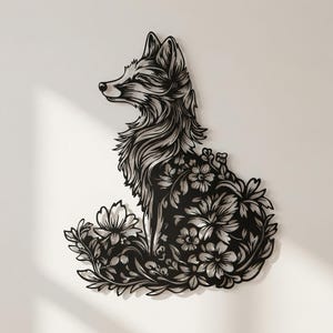 May include: Black metal fox wall art with intricate floral detailing. The fox is depicted in a seated position, with its body and the surrounding foliage cut out to create a negative space effect. The artwork is designed to be mounted on a wall.